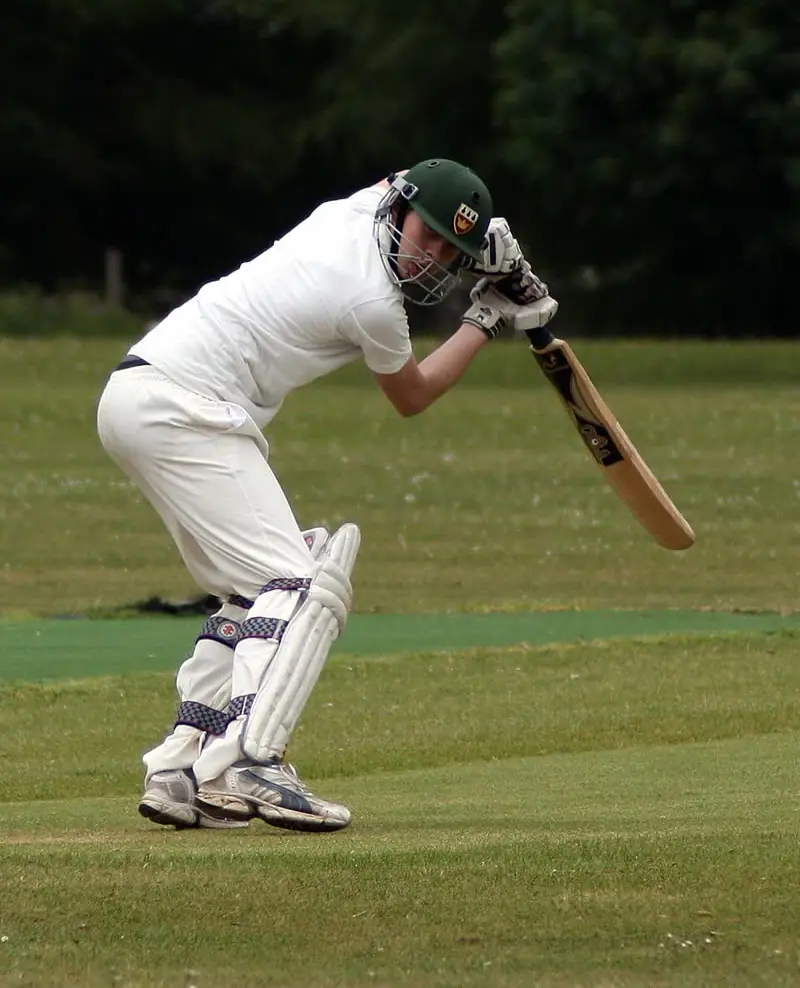 A club batter in whites at the crease, bat raised, during a village match